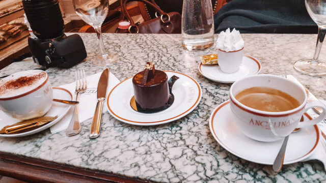 Table setting at Angelina Paris with signature hot chocolate, cappuccino, espresso with whipped cream, and a rich chocolate dessert on a marble table.