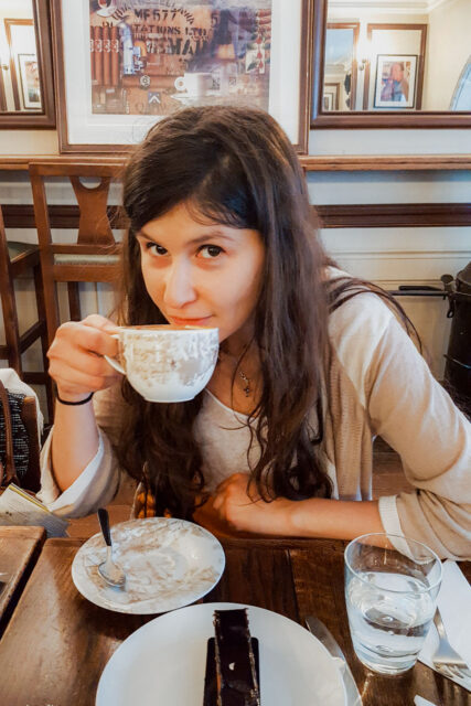 Woman drinking coffee at Café Verlet in Paris, France, with a chocolate dessert on the table and elegant vintage décor in the background.