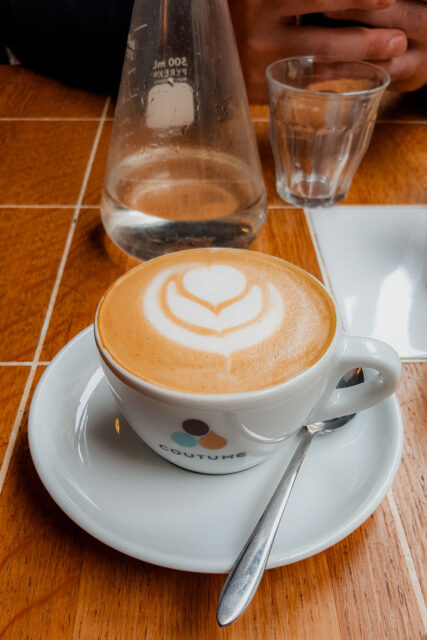 Cappuccino with heart-shaped latte art served in a Coutume Café cup on a wooden table in Paris, France.