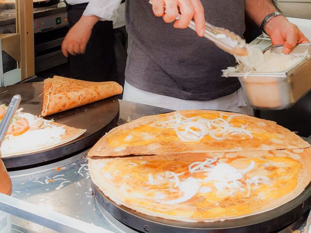 Close-up of a chef preparing fresh savory crepes on a hot griddle in Paris, adding sliced onions and cheese as filling.