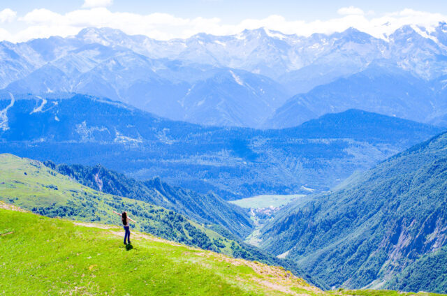 Woman standing on a grassy ridge in Svaneti, Georgia, with breathtaking views of the Caucasus Mountains and deep blue valleys in the background.
