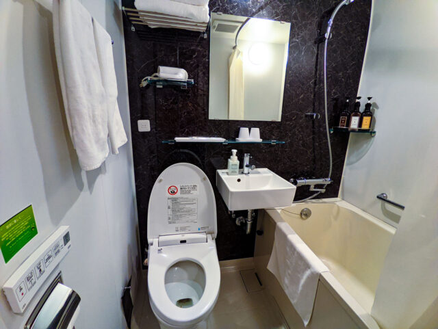 Compact Japanese hotel bathroom with bidet toilet, sink, and shower-bathtub combination. At the Henn-na Hotel Tokyo Akasaka
