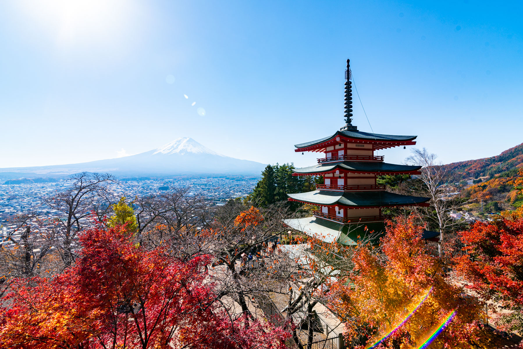 Chureito Pagoda framed by vibrant autumn leaves with snow-capped Mount Fuji in the background on a clear, sunny day in Fujiyoshida, Japan.