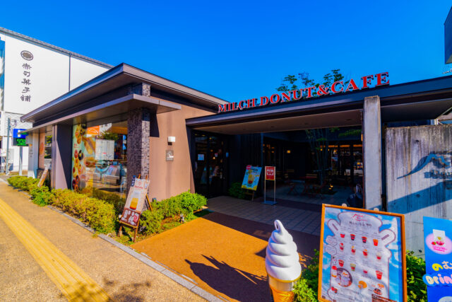 Exterior of Milch Donut & Café in Yufuin, Japan, with colorful signs and a soft serve display under clear blue skies.