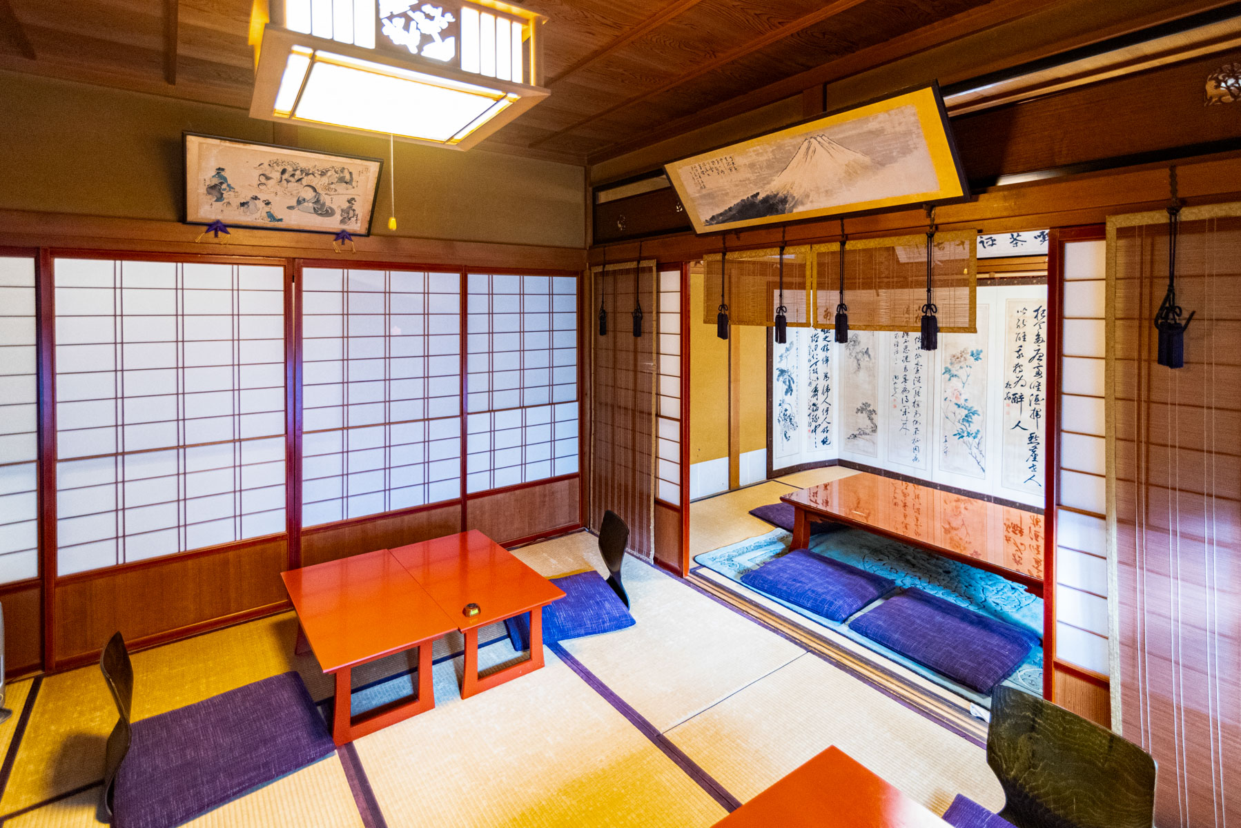 Traditional Japanese interior at Fukuyan Café in Takayama, featuring tatami mats, low lacquered tables with floor cushions, sliding shoji doors, and hanging scrolls with calligraphy and artwork.