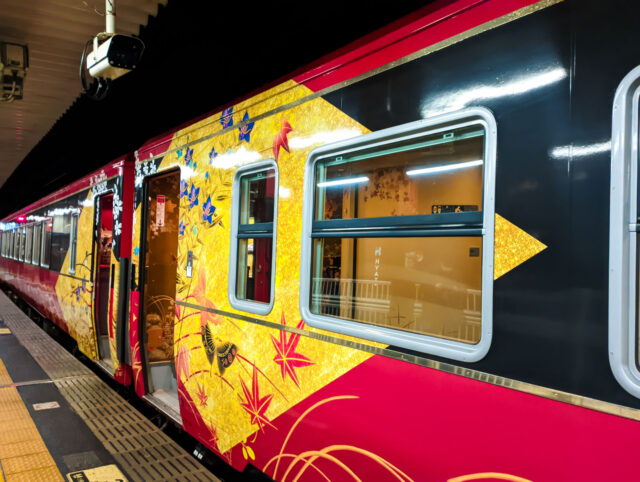 Exterior of the Hanayome Noren sightseeing train in Kanazawa, featuring elegant red, black, and gold colors with floral and seasonal designs inspired by local culture.