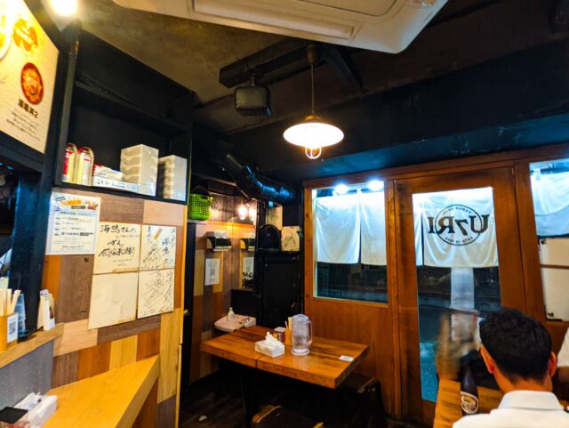 Cozy Japanese izakaya interior with wooden tables, signed shikishi boards on the wall, and warm lighting in Fukuoka.