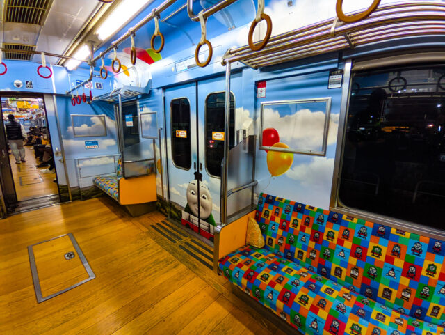 Interior of the Thomas the Tank Engine-themed train on the Fujikyu Railway Kawaguchiko Line, featuring Thomas’ smiling face on the door, colorful balloon artwork, and patterned seats decorated with characters from the series.