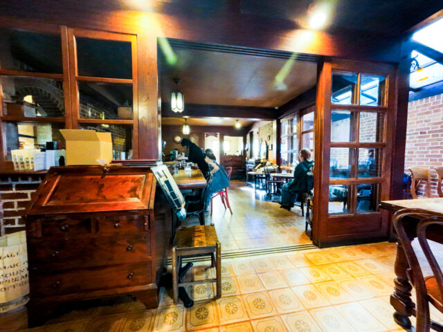 Interior of Kurashiki Coffee Kan, featuring wooden furniture, vintage decor, brick walls, and warm lighting with customers seated at tables and the counter.