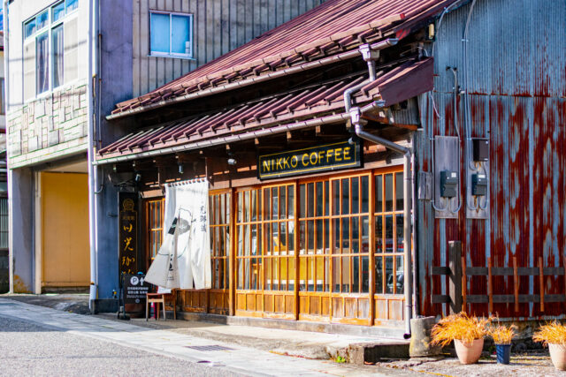 Exterior of Nikko Coffee, a rustic café in Nikko with wooden sliding doors, a fabric curtain at the entrance, and a traditional tiled roof.