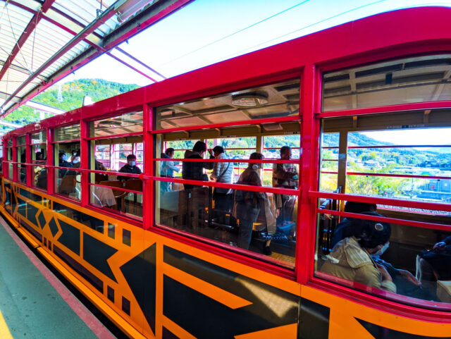 Bright red Sagano Romantic Train Rich Car carriage in Kyoto with open windows, offering passengers panoramic views of the surrounding mountains and rivers