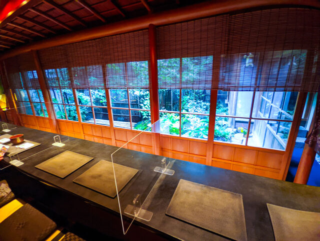 Interior of Shima Teahouse in Kanazawa - inside a historic geisha house, with tatami seating, counter tables, and a view of the garden through traditional wooden windows.