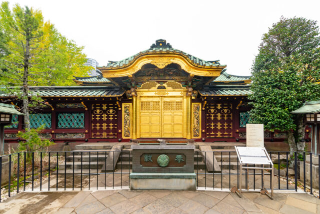 Ornate golden gate of Ueno Toshogu Shrine with intricate carvings and green-tiled roof, framed by trees in Ueno Park, Tokyo.