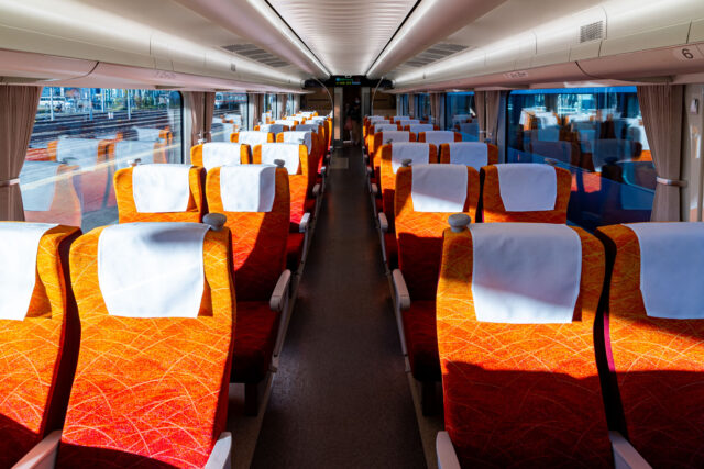 Interior of the Wide View Hida Limited Express train on the Takayama to Osaka route, featuring bright orange seats with white headrests and large panoramic windows designed for enjoying scenic mountain and countryside views.