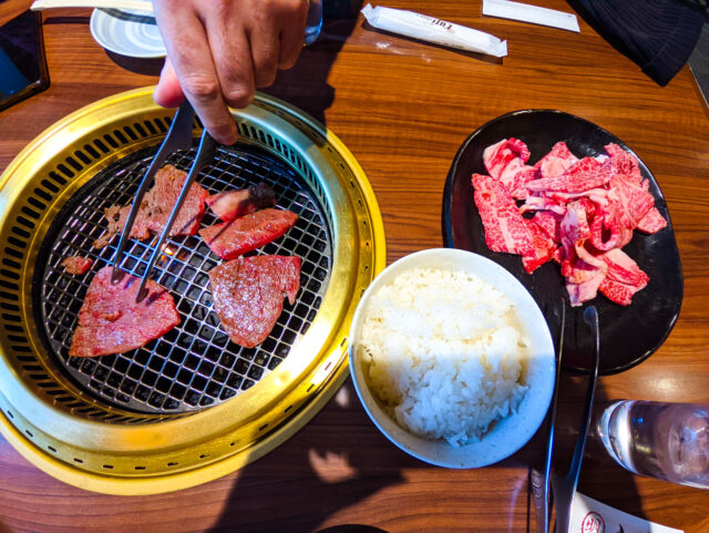 Premium Wagyu beef grilling on a golden yakiniku grill in Takayama, served with white rice and a plate of raw marbled meat.