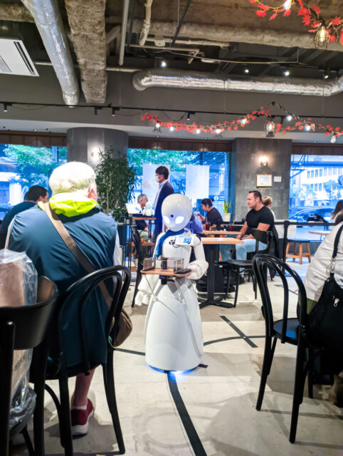 Robot waiter navigating the tables filled with customers, serving drinks at Dawn Café in Tokyo Japan, a futuristic café where humanoid service robots assist customers.