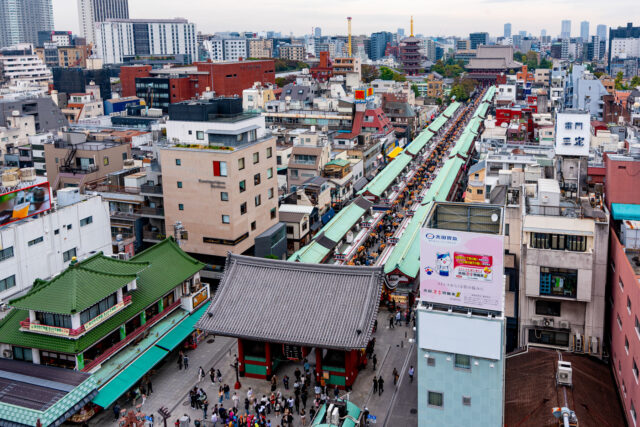 View from Asakusa Tourist Information Center overlooking the bustling Nakamise Shopping Street leading to Sensoji Temple in Tokyo, lined with green-roofed stalls and filled with visitors.