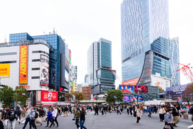 Crowds of people crossing at Shibuya Scramble Crossing in Tokyo Japan, surrounded by modern skyscrapers, billboards, and neon signs.