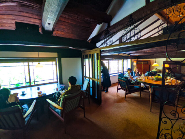 Interior of Café Tenjosajiki, Yufuin—cozy upstairs room with exposed wooden beams, low windows, pendant lights, and guests at round tables.