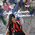 Portrait of a woman at a trendy Busan cafe, sitting by a neon sign and floral wall, in a red and black outfit.